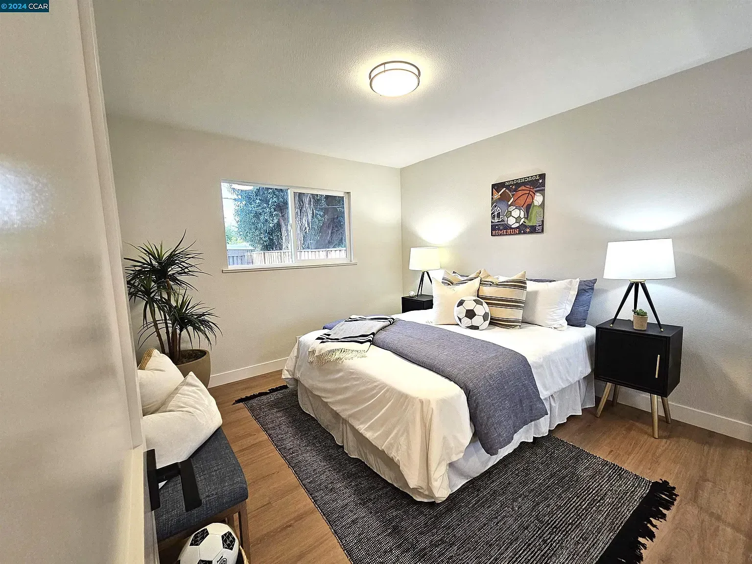 Bedroom with a bed, nightstands, rug, and a bench. Features a window, plant, and artwork.