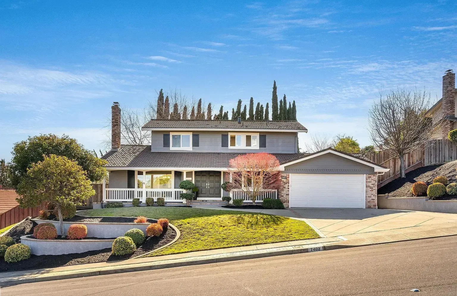 Two-story gray house with white trim, garage, and landscaped yard on a sunny day.