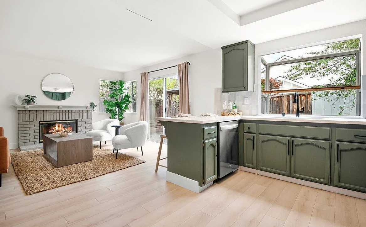 Open-concept kitchen and living area with a fireplace. Olive green kitchen cabinets and sliding door to a backyard.