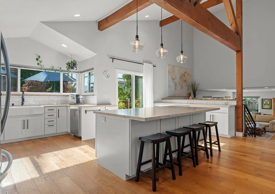 Spacious kitchen with gray island, stools, light wood floors, and exposed wooden beams.