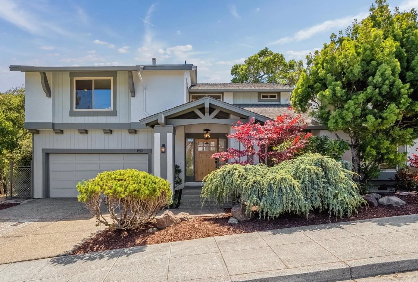 Two-story house with beige siding, a garage, and landscaped front yard with colorful plants.