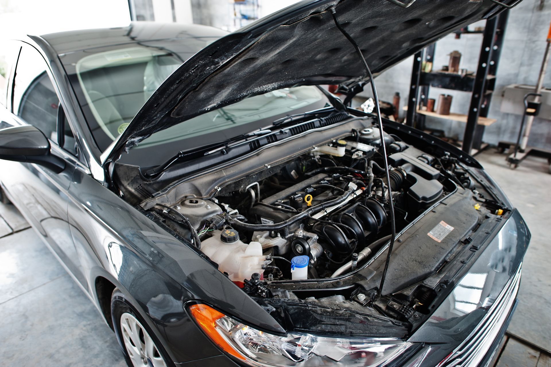 Black car with hood open, showing engine in a garage.