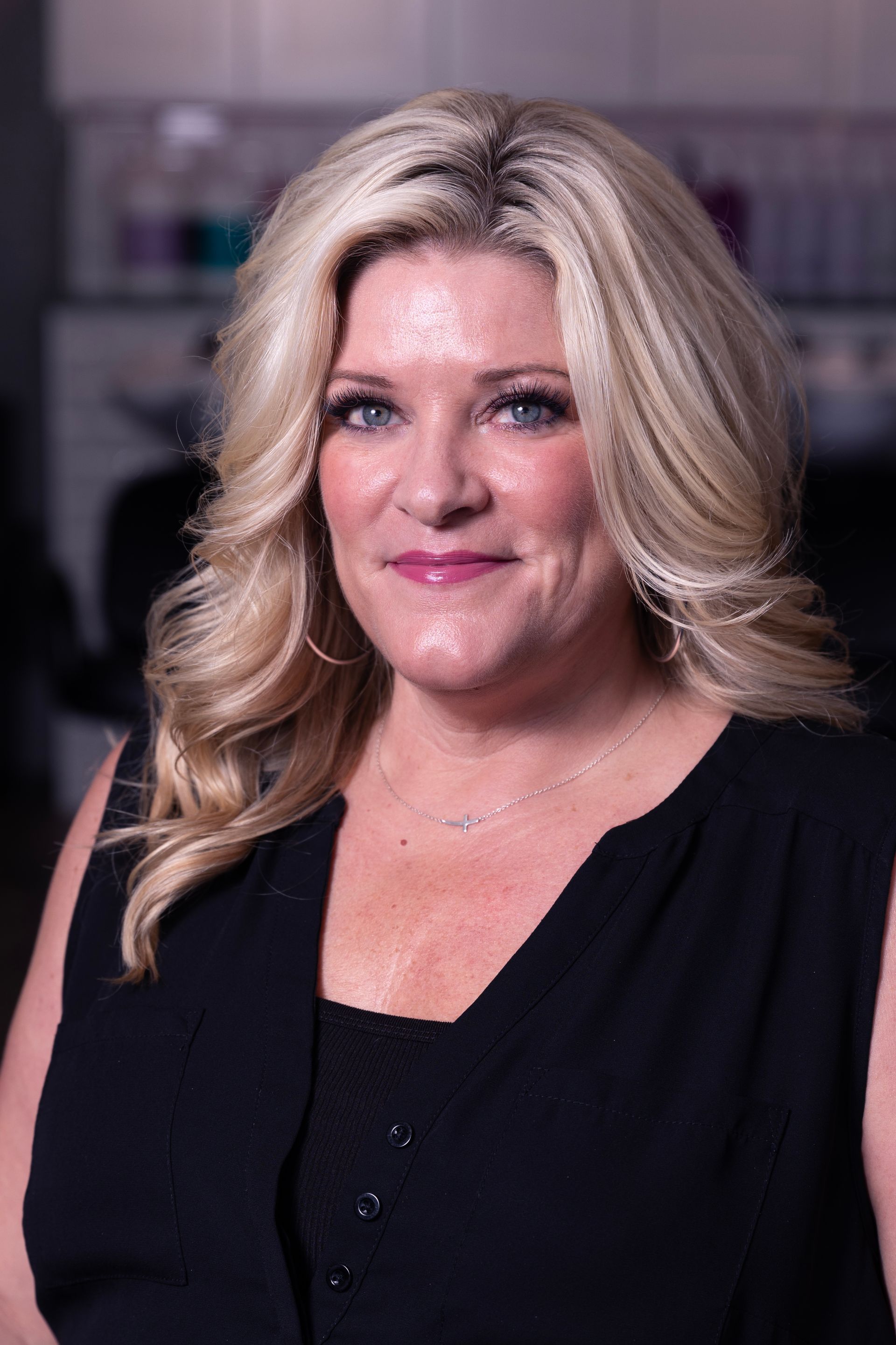 Woman with blonde wavy hair, wearing a black top, smiling, indoors.