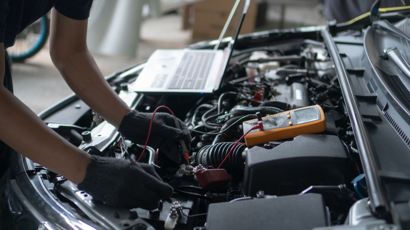 Mechanic using a multimeter and laptop to diagnose a car engine.