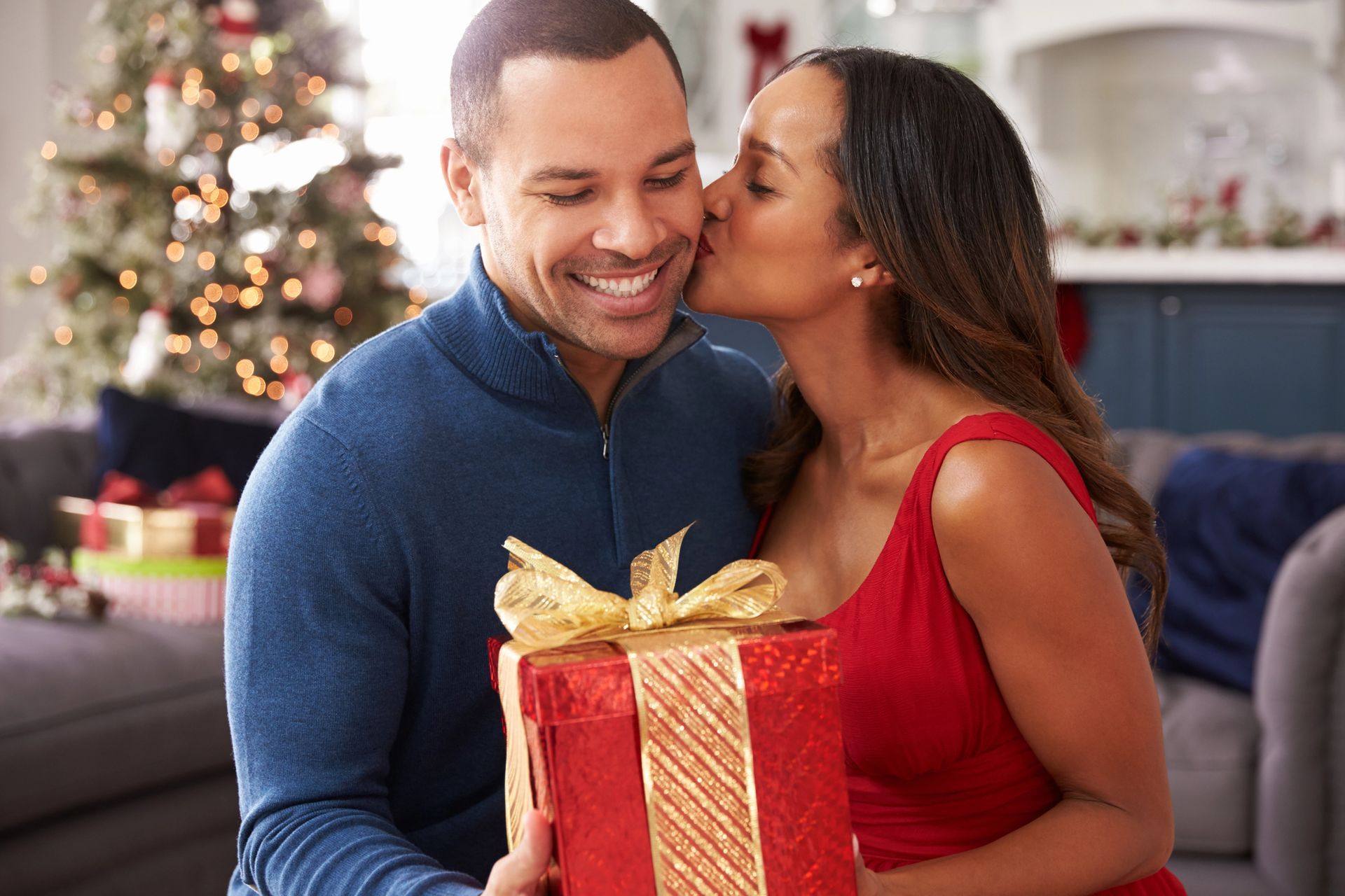 A woman is kissing a man on the cheek while holding a Christmas present.
