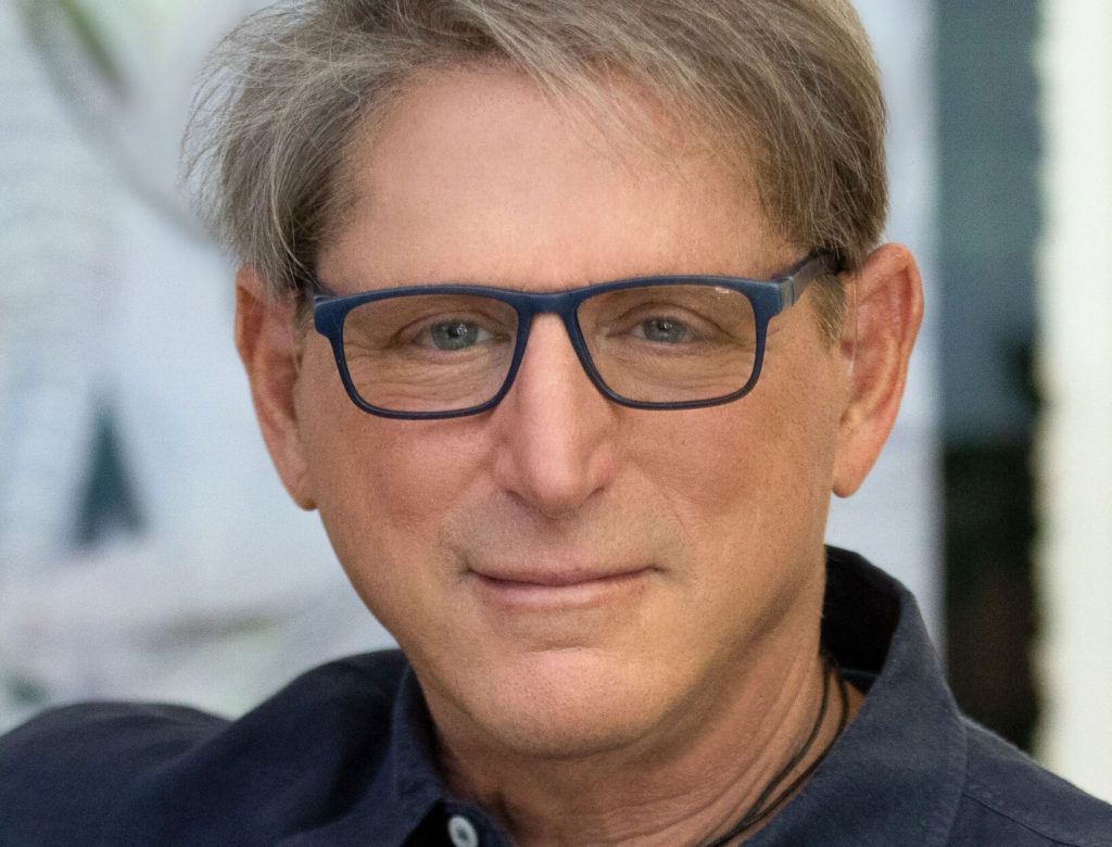 A man wearing glasses and a blue shirt is smiling for the camera.