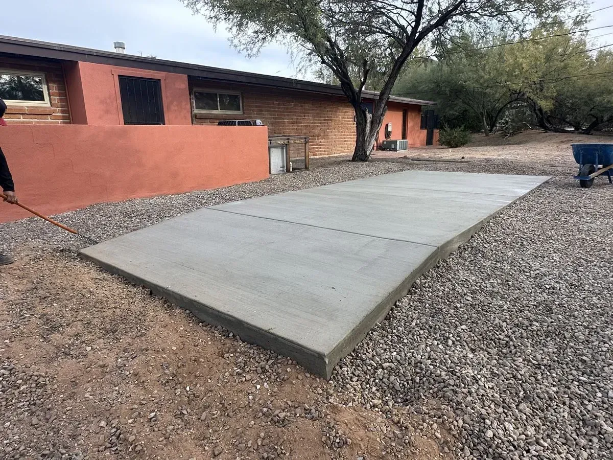 Freshly poured concrete patio surrounded by gravel; adjacent to a red stucco building.
