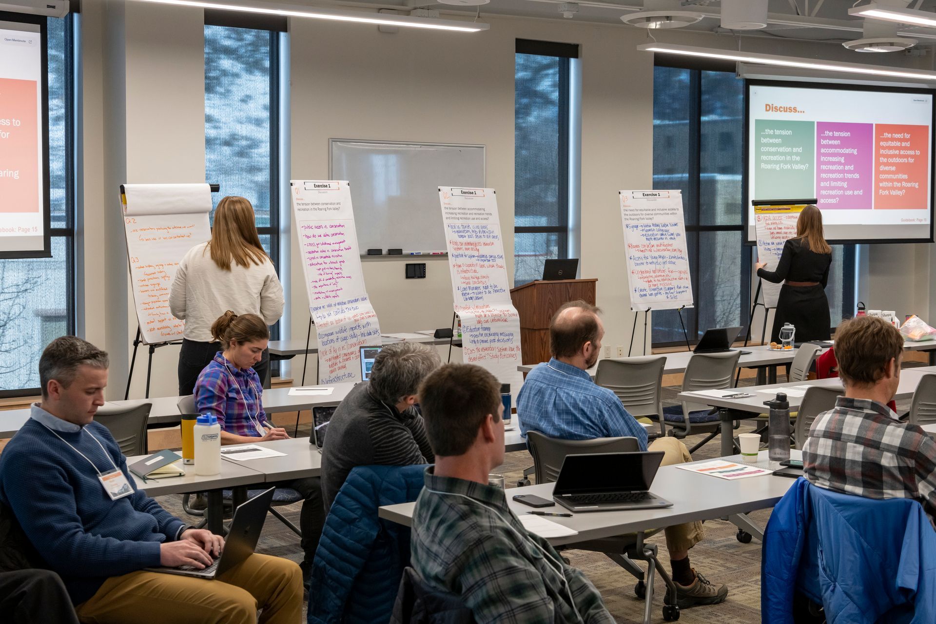 People working in a classroom with whiteboard easels, projectors, and tables in roaring fork colorado