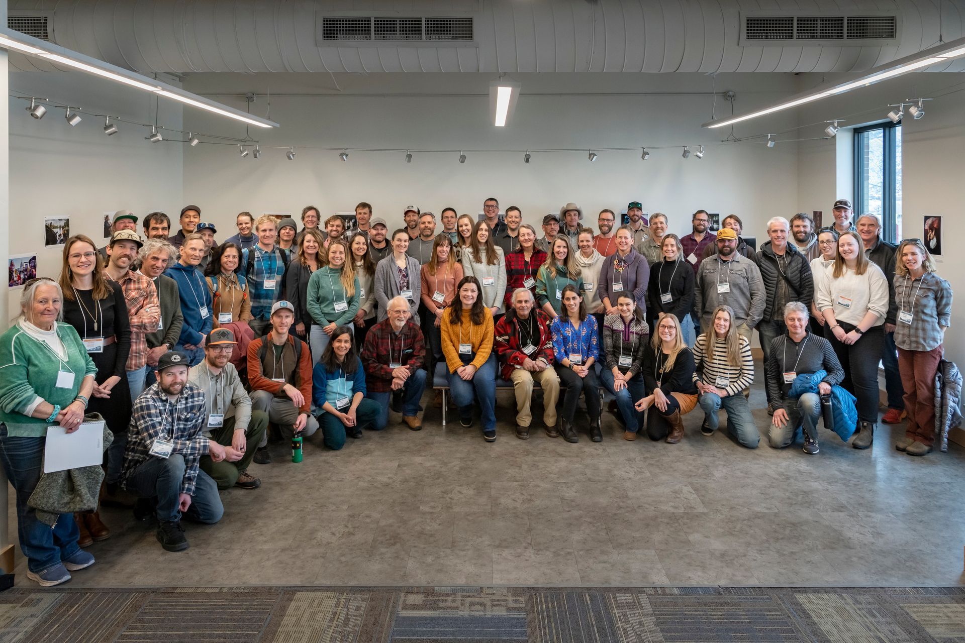 A large, diverse group of people posing for a group photo in a brightly lit room with white walls and a carpeted floor in roaring fork colorado