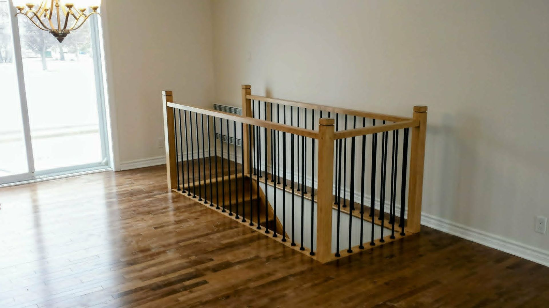 Rambarde d'escalier en bois entourant une cage d'escalier ouverte dans une pièce lumineuse et vide avec parquet.