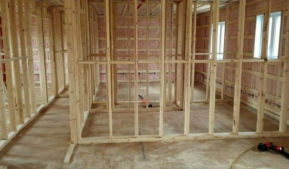 Intérieur à ossature bois d'une maison en construction, avec montants apparents et plancher non fini.