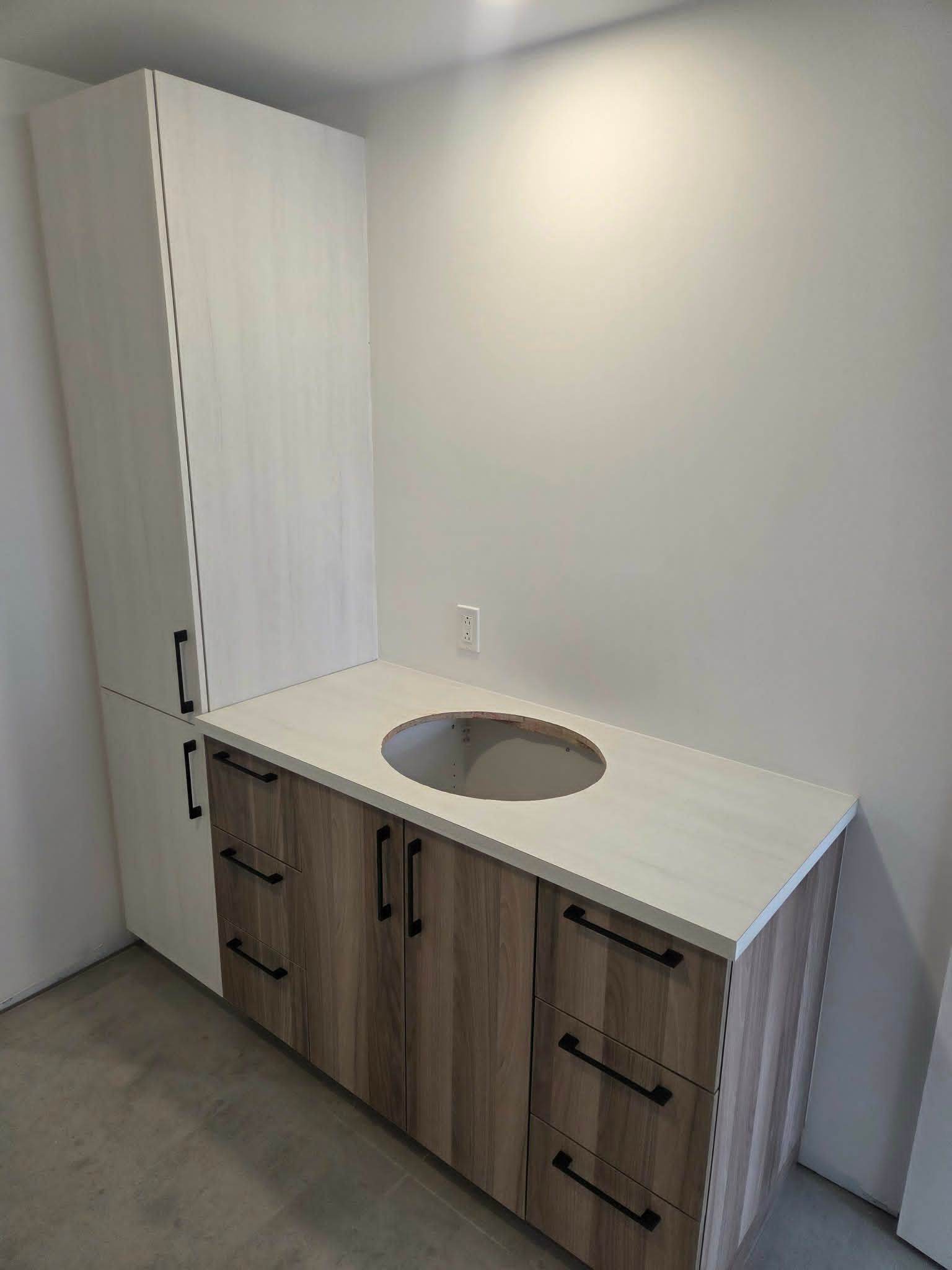 Aménagement d'une petite cuisine avec un plan de travail blanc, un évier rond encastré et une armoire haute dans une pièce grise