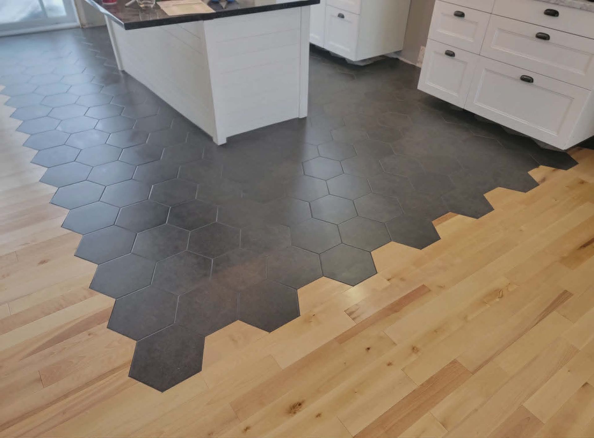 Sol de cuisine avec incrustation de carreaux hexagonaux noirs entre le parquet clair et les meubles blancs.