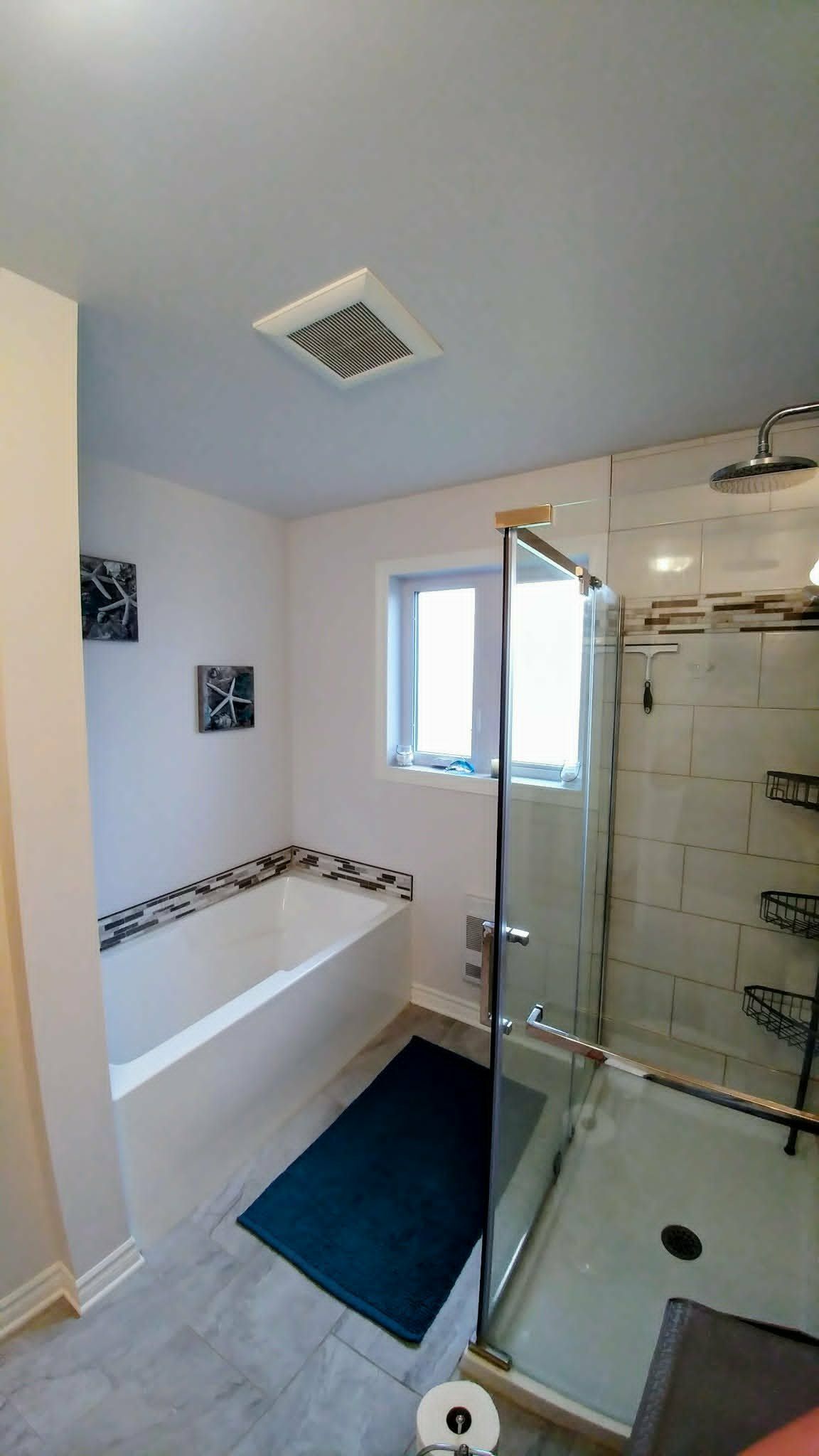 Petite salle de bains avec baignoire, douche en verre, fenêtre et tapis de bain bleu marine.