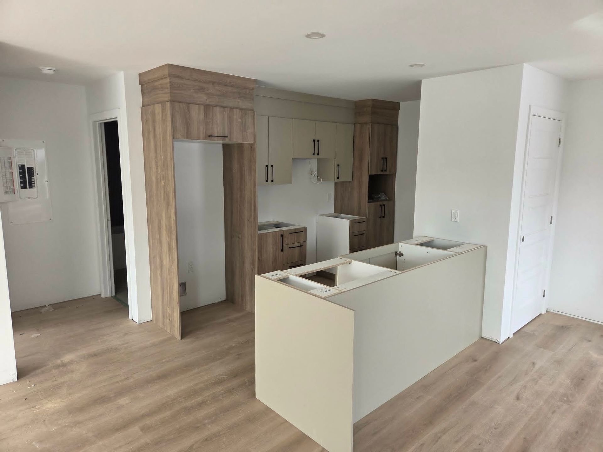 Cuisine moderne vide avec parquet clair, placards blancs et îlot central dans une pièce ouverte et lumineuse