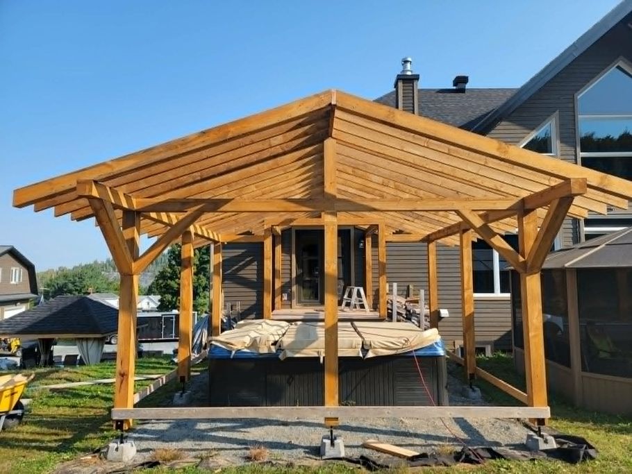 Un kiosque en bois avec un jacuzzi est en construction dans une cour arrière, couvert de poutres en bois clair.