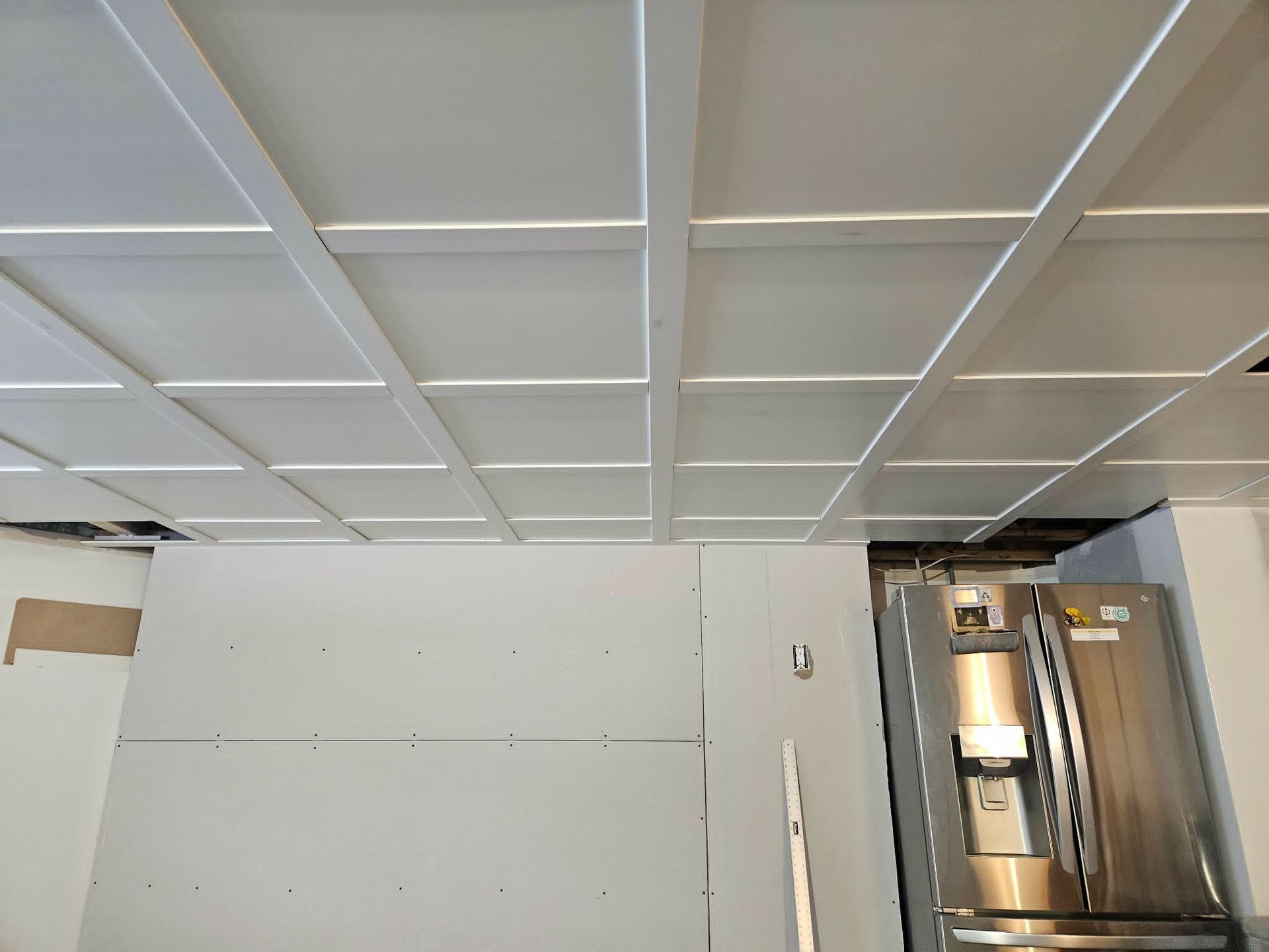 Intérieur en travaux avec panneaux de plafond blancs, mur non fini et porte ouverte donnant sur la buanderie