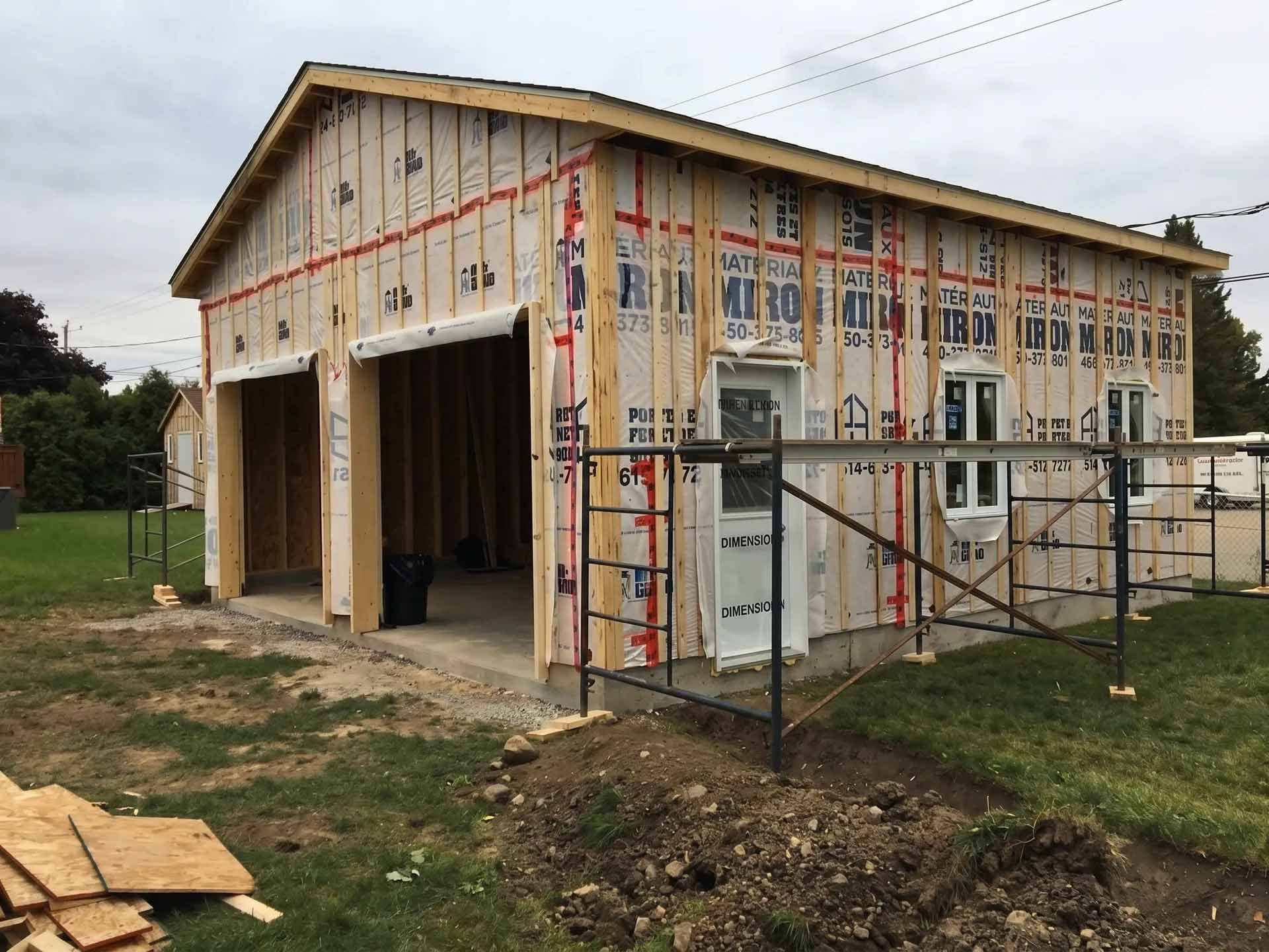 Abri partiellement construit avec charpente apparente, porte ouverte de type garage et matériaux de construction à l'extérieur.