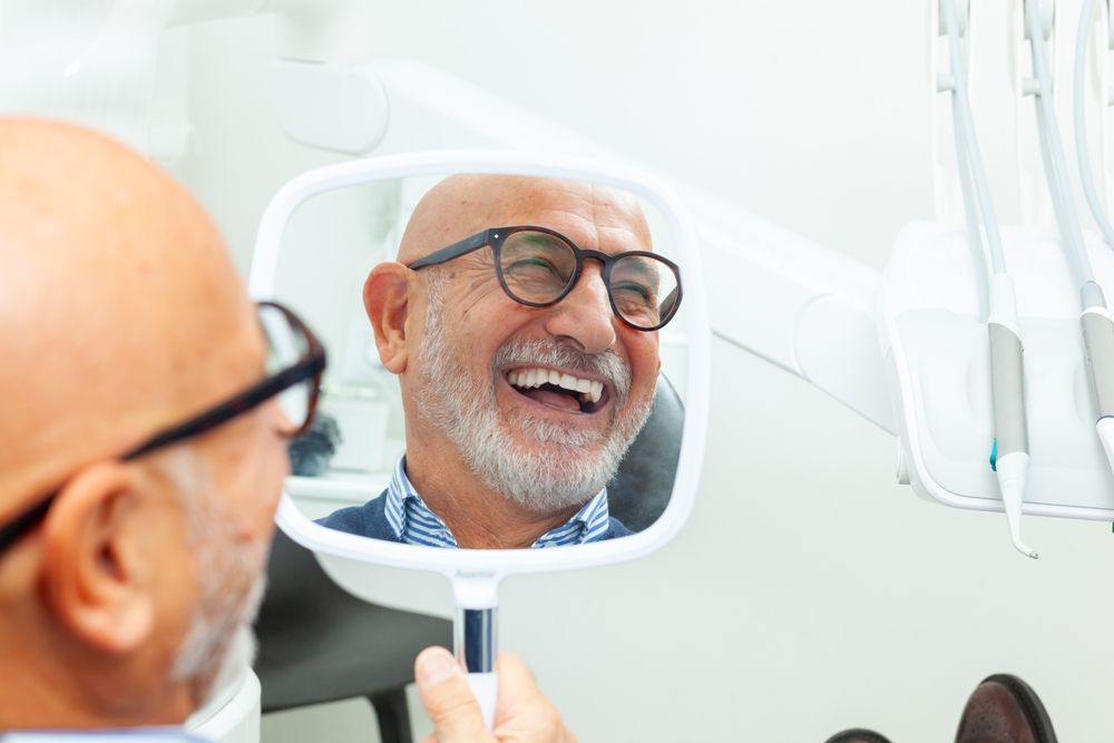 Man looking at his teeth in a mirror, smiling widely, in a dental office. — McDonald Dental in Gympie, QLD