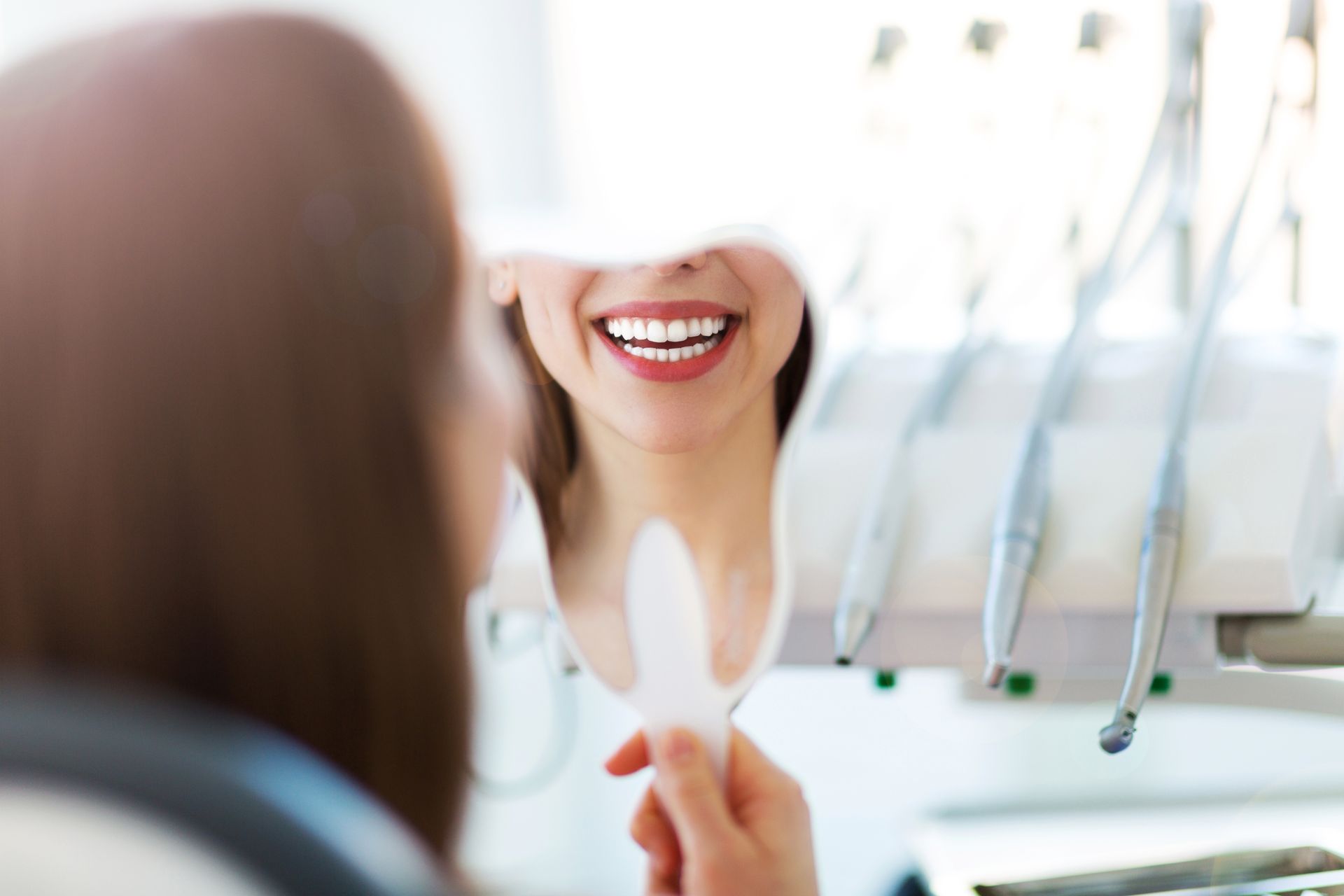Woman smiles at her teeth in a dentist's mirror, dental tools in the background. — McDonald Dental in Gympie, QLD