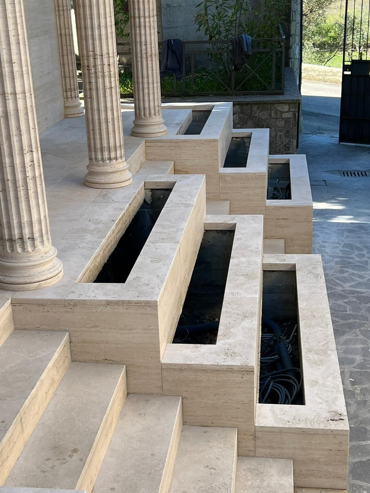Fontana a gradoni in pietra accanto a un portico con colonne bianche e lunghe vasche rettangolari