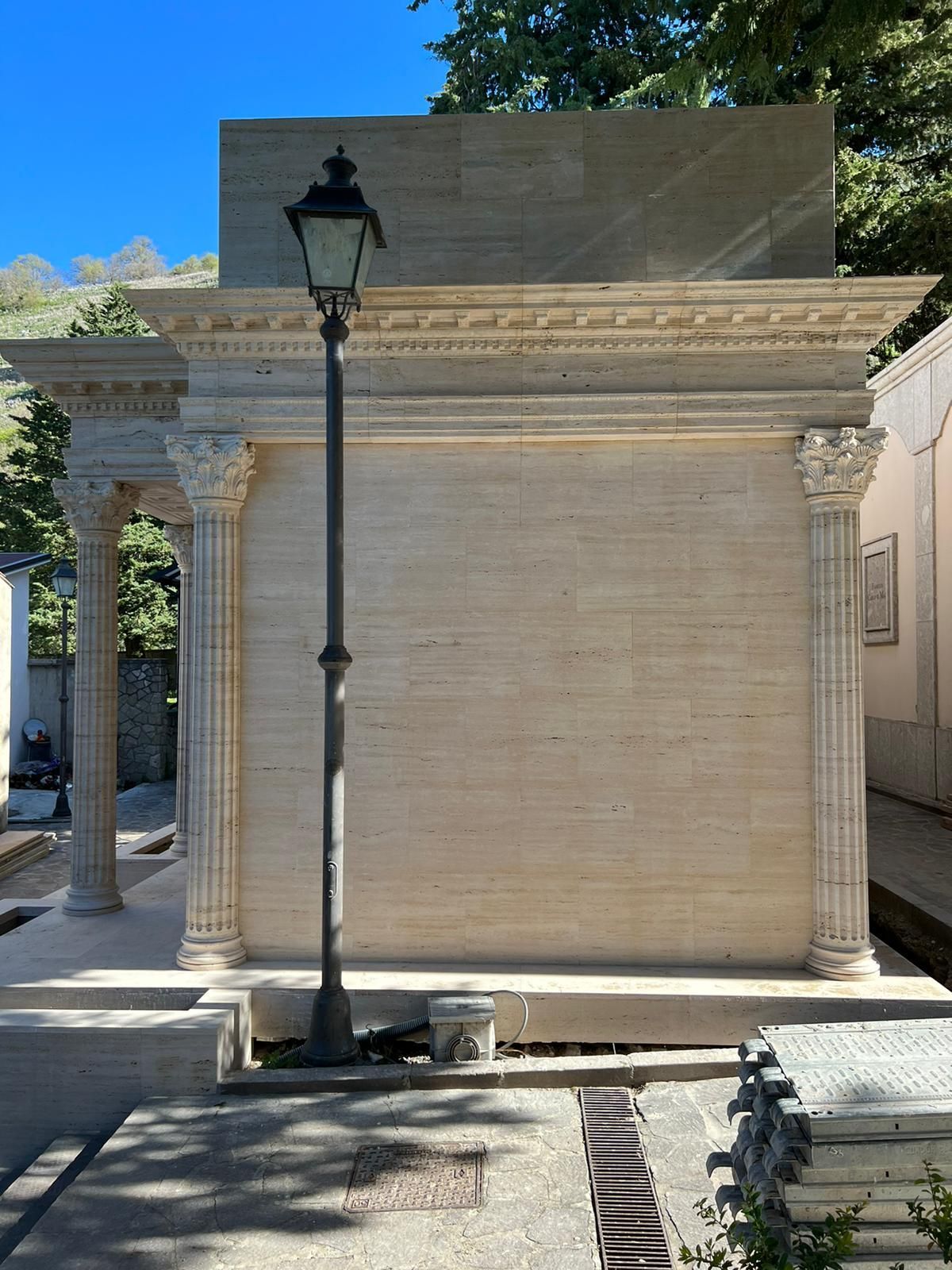 Mausoleo in pietra con tetto piatto e lampione nero antistante, all'aperto, esposto alla luce del sole.