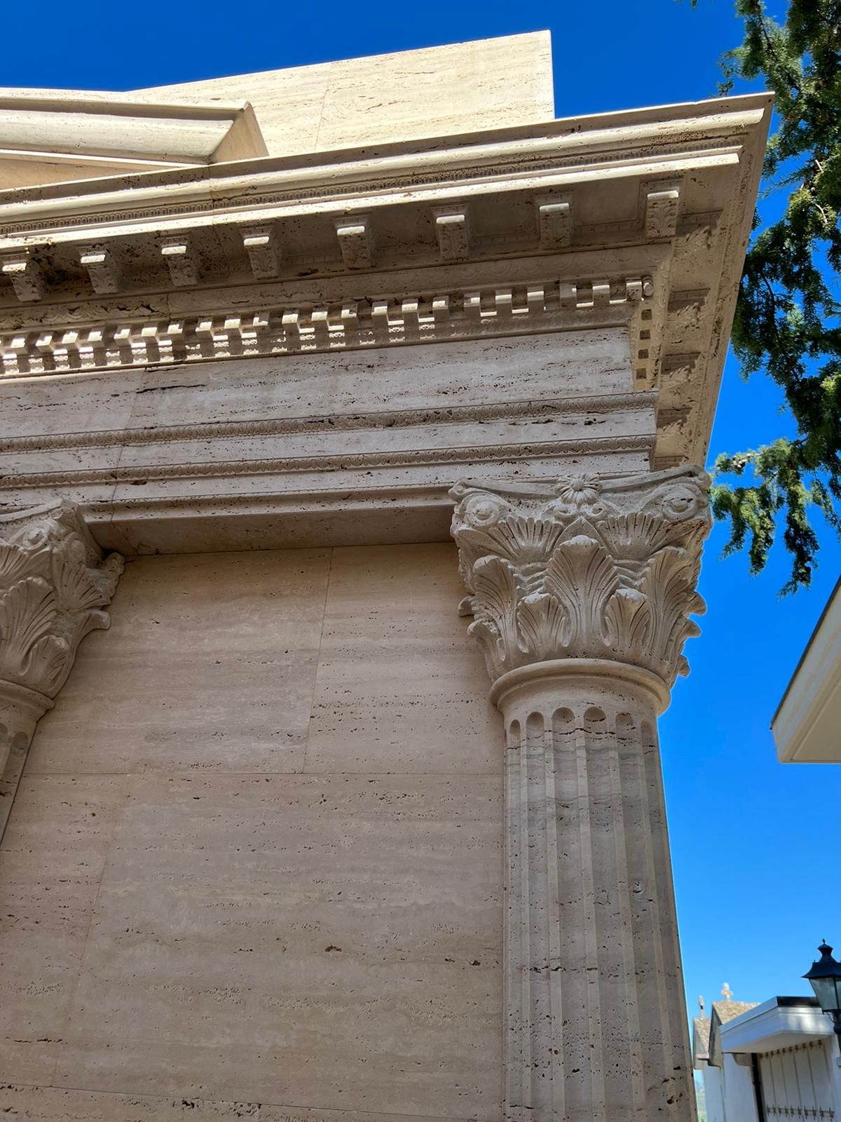 Facciata in pietra riccamente decorata con colonne e cornicione scolpiti, sullo sfondo di un cielo azzurro brillante.