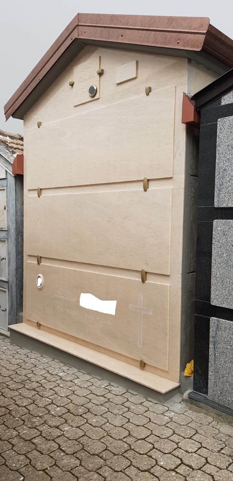 Armadietto di servizio in legno con tetto spiovente accanto a un muro di pietra su un vialetto lastricato.