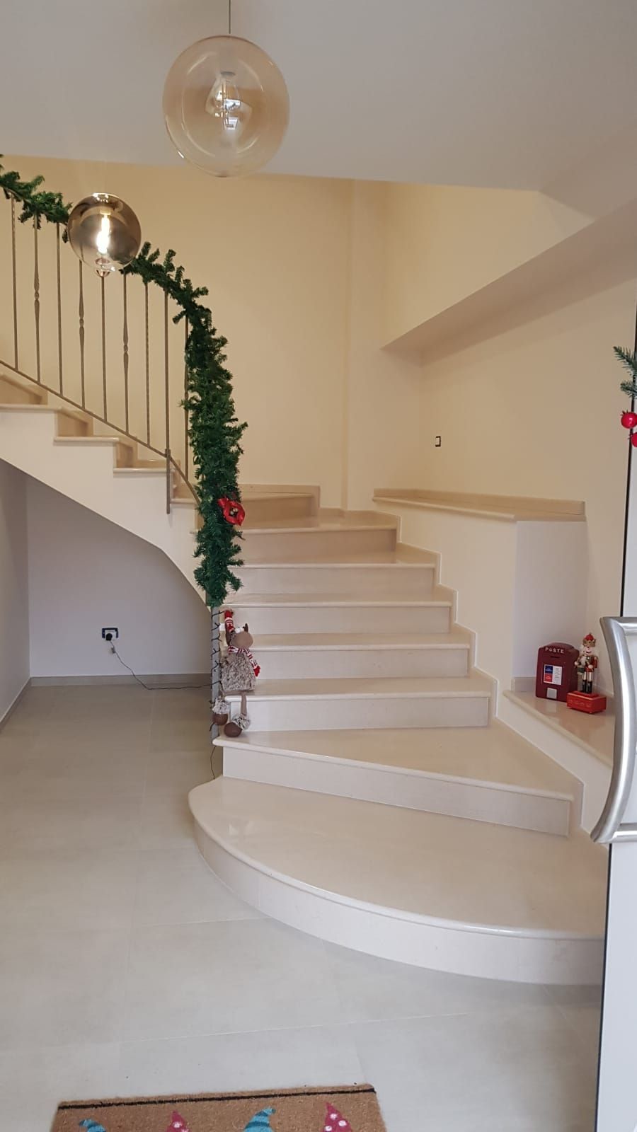 Scala curva con gradini rivestiti di moquette beige e ringhiera decorata con ghirlande verdi in un luminoso atrio.