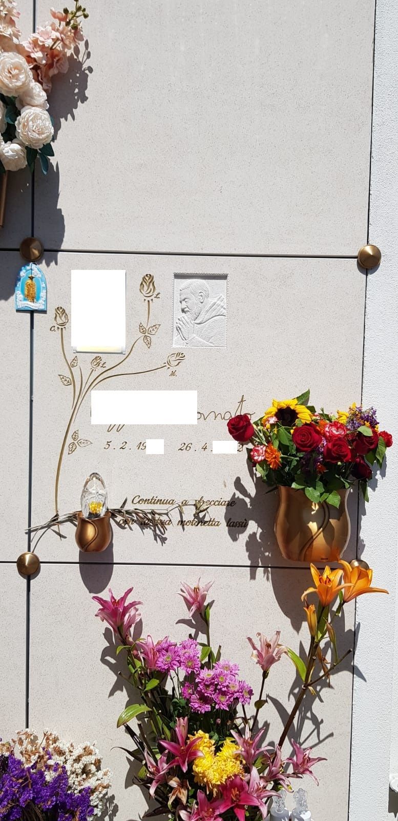 Targa commemorativa su un muro, circondata da composizioni floreali e bouquet colorati.
