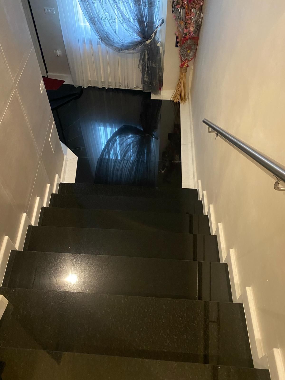 Scala con gradini scuri e lucidi, pareti bianche e corrimano che conduce a un pianerottolo con tenda.
