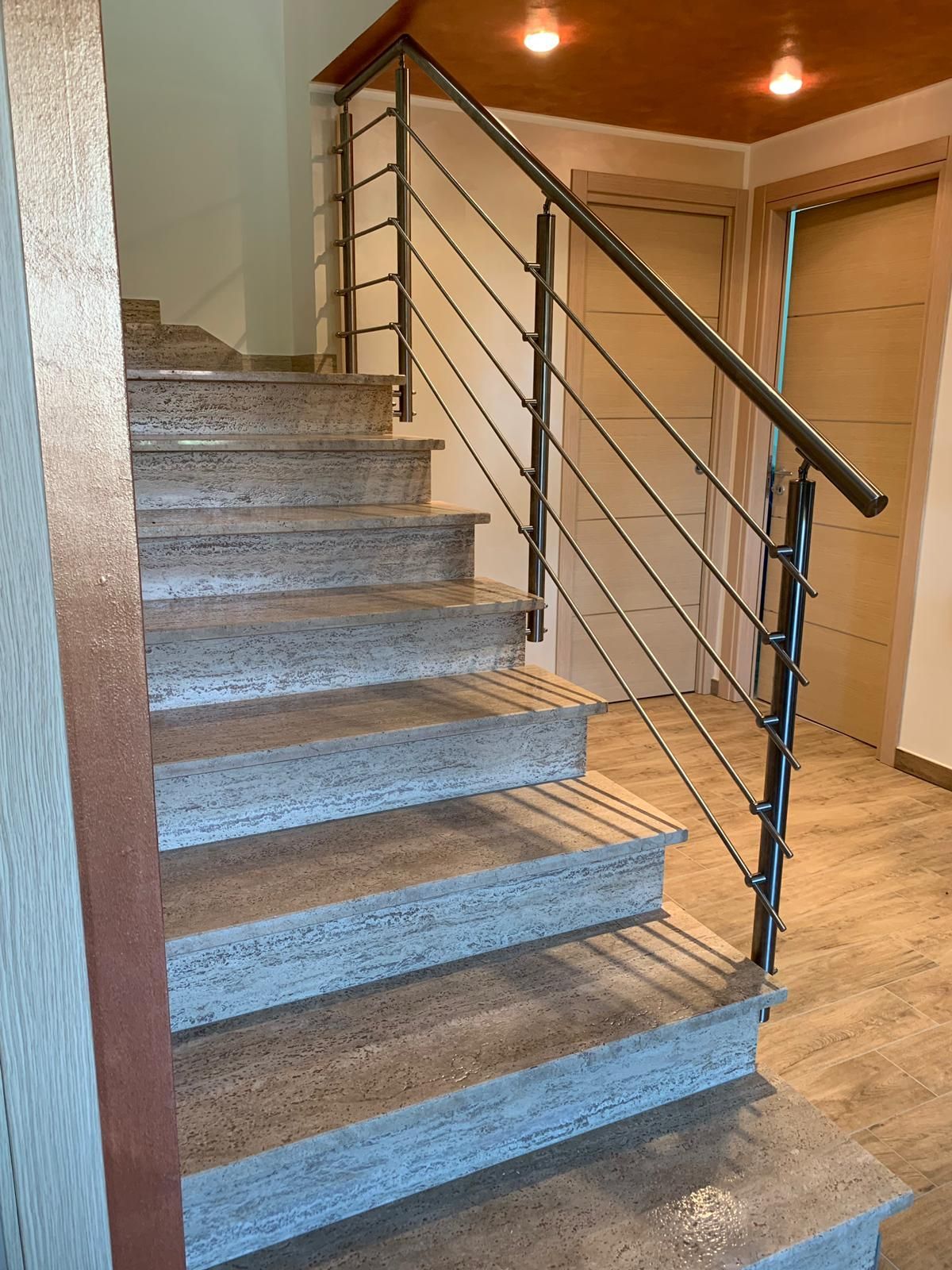 Scala interna rivestita di moquette con ringhiera in metallo e illuminazione calda in un corridoio beige.