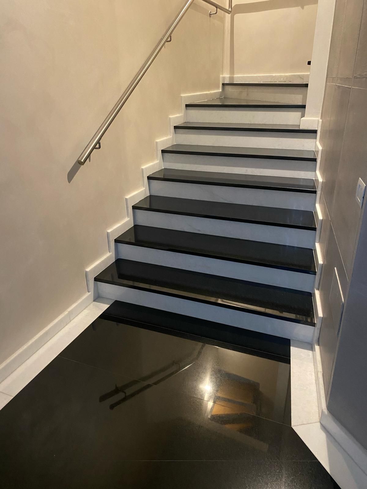 Scala interna con gradini scuri, pareti bianche e corrimano in metallo sulla sinistra.