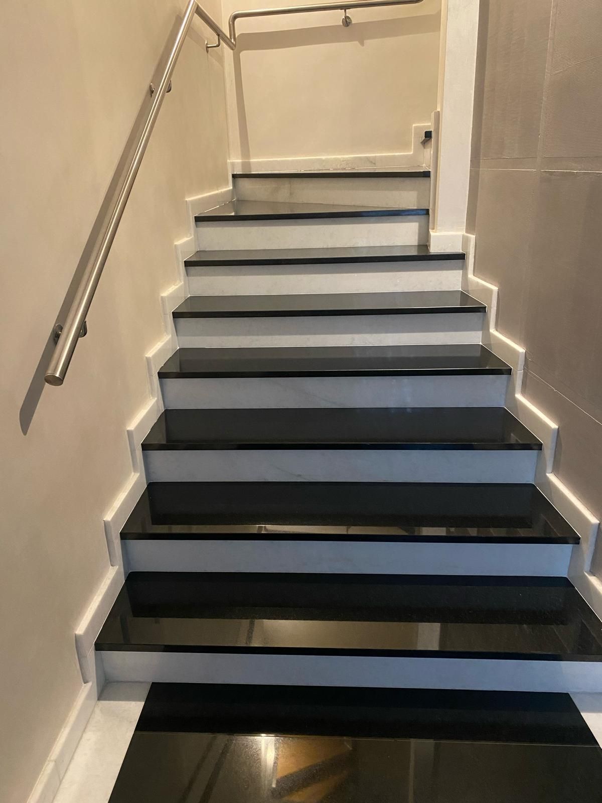 Scala interna con gradini grigi, pareti beige e corrimano in metallo che sale verso l'alto.