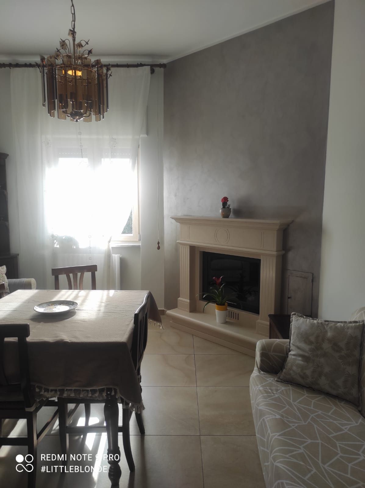 Luminosa sala da pranzo con tavolo, sedie, finestra, lampadario e camino sulla destra.