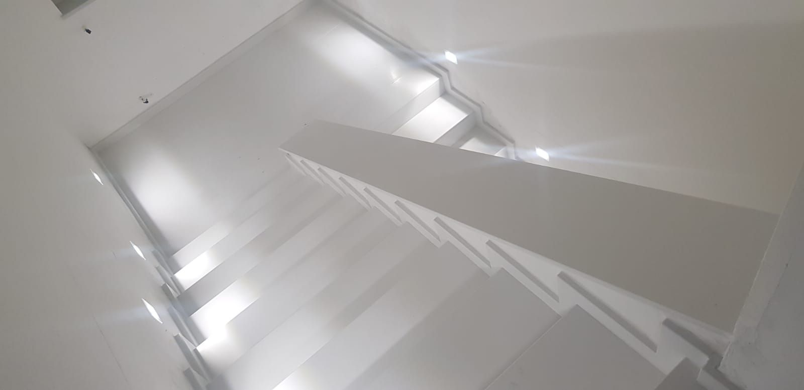 Vano scale bianco visto dall'alto, con luci brillanti e ringhiere geometriche