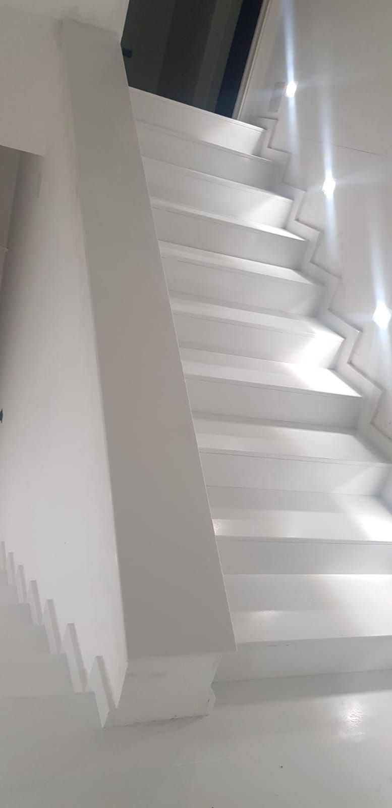 Scala bianca con gradini angolari e luce brillante che si riflette sulle pareti lucide