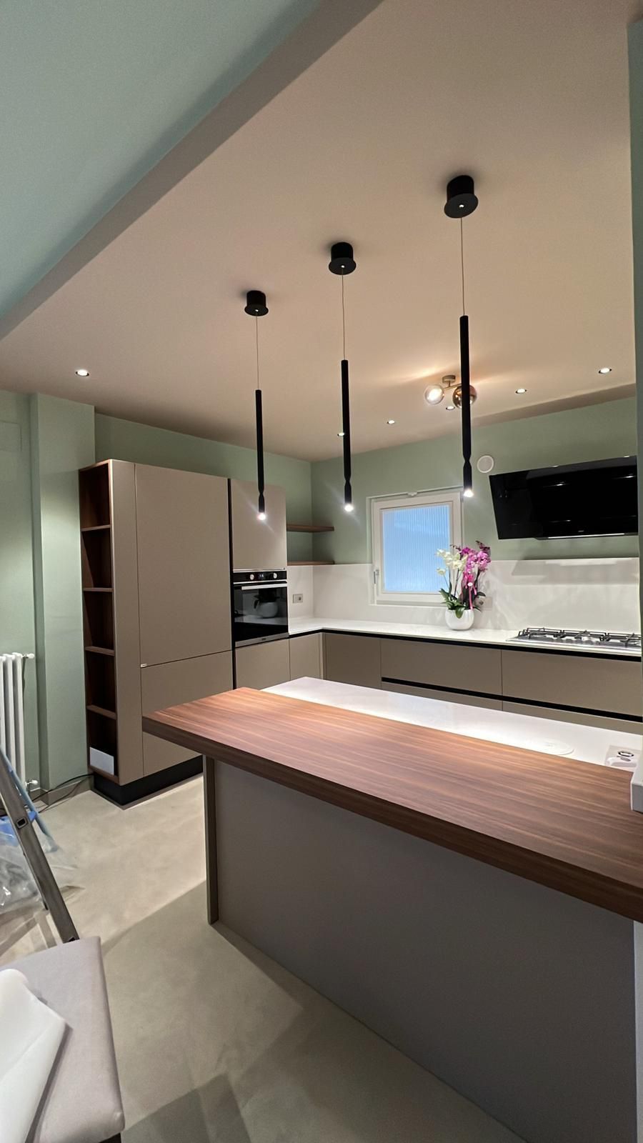 Cucina moderna con isola in legno, frigorifero in acciaio inox, lampade a sospensione e mobili bianchi.