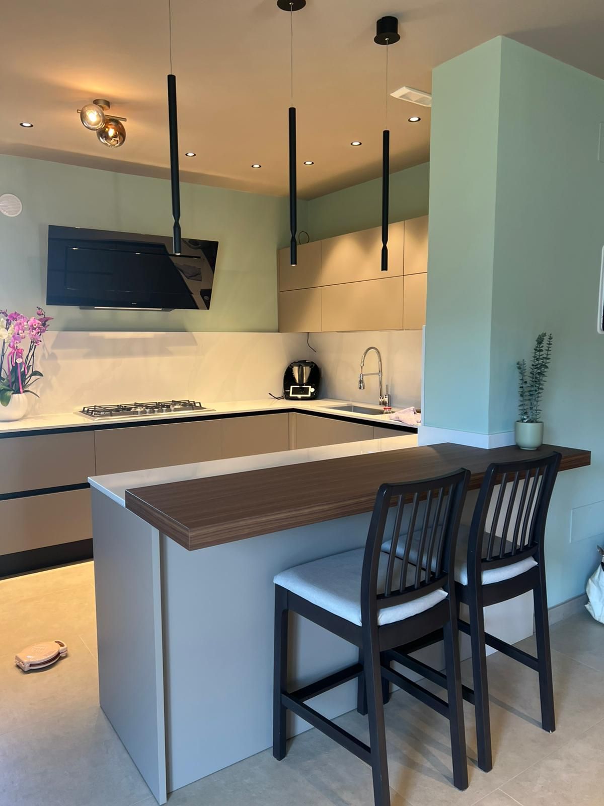 Cucina moderna con isola, piano di lavoro in legno, sgabelli da bar neri ed elettrodomestici a incasso.