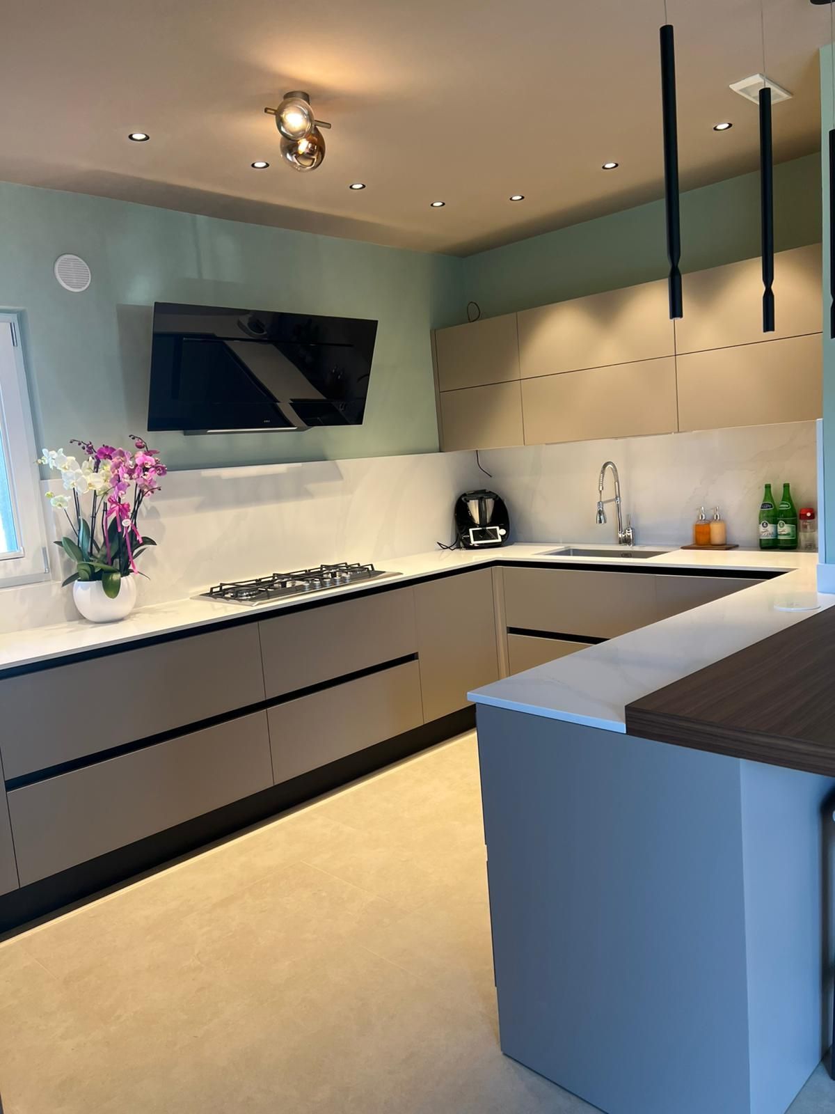 Cucina moderna grigia con ripiani bianchi, elettrodomestici neri, lampade a sospensione e isola centrale.