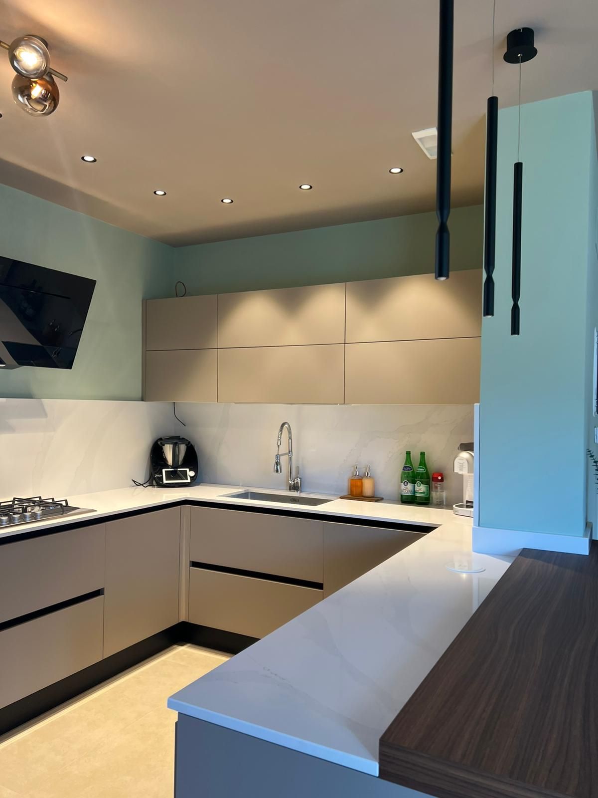 Cucina moderna e minimalista con mobili grigi, ripiani bianchi e illuminazione a soffitto dai toni caldi.