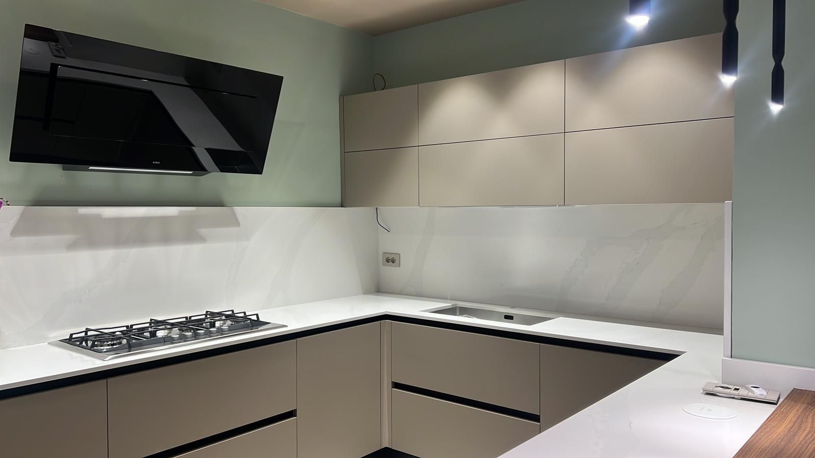 Cucina moderna bianca con elettrodomestici a incasso, piano cottura a gas e mobili beige con illuminazione a incasso.