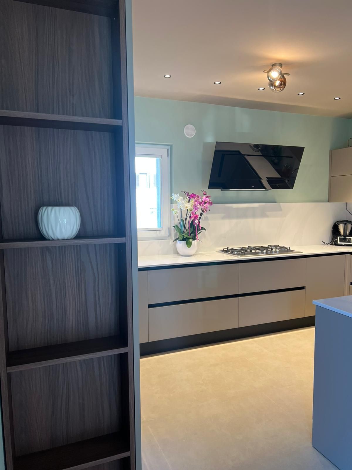 Cucina moderna con scaffalature scure, isola bianca e fiori rosa sul bancone.