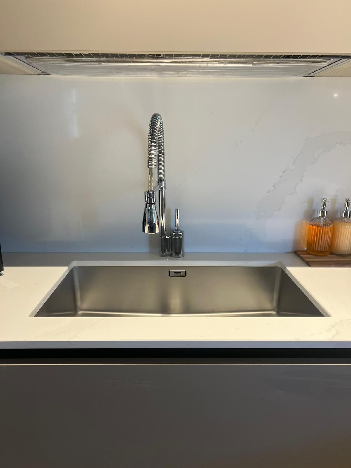 Lavello da cucina moderno con rubinetto cromato, piano di lavoro bianco e vassoio di arance sulla destra.