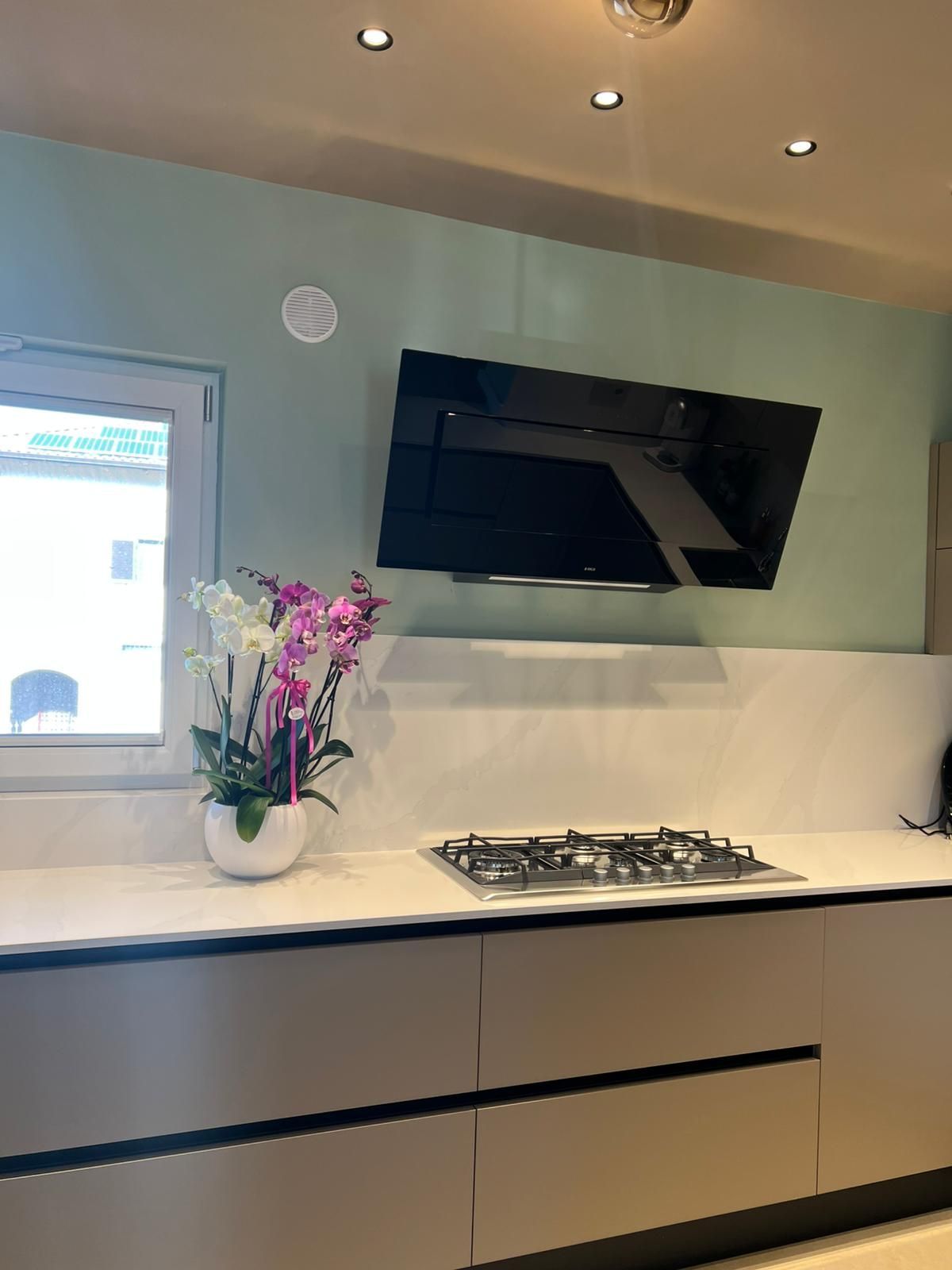 Cucina moderna con ripiani bianchi, cappa nera, piano cottura a gas e un vaso di fiori rosa.
