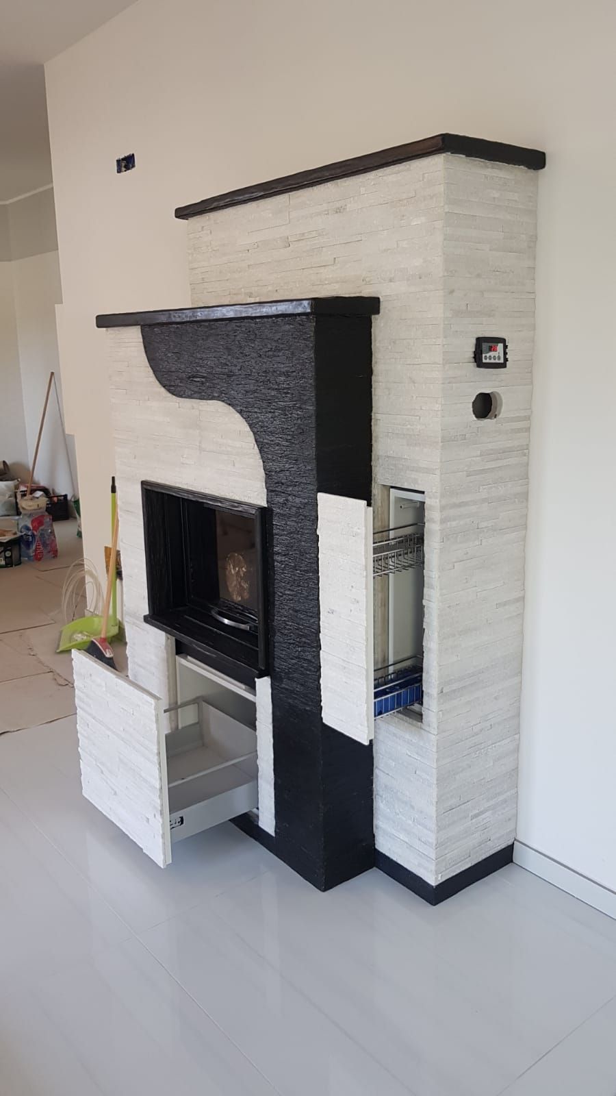 Camino moderno in bianco e nero con mensola per la TV e rivestimento in piastrelle in una stanza luminosa.