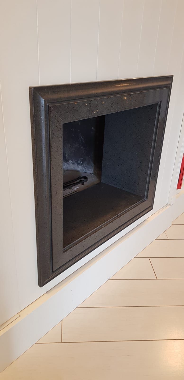 Inserto per camino a parete di colore nero in una stanza bianca con pavimento in legno chiaro.