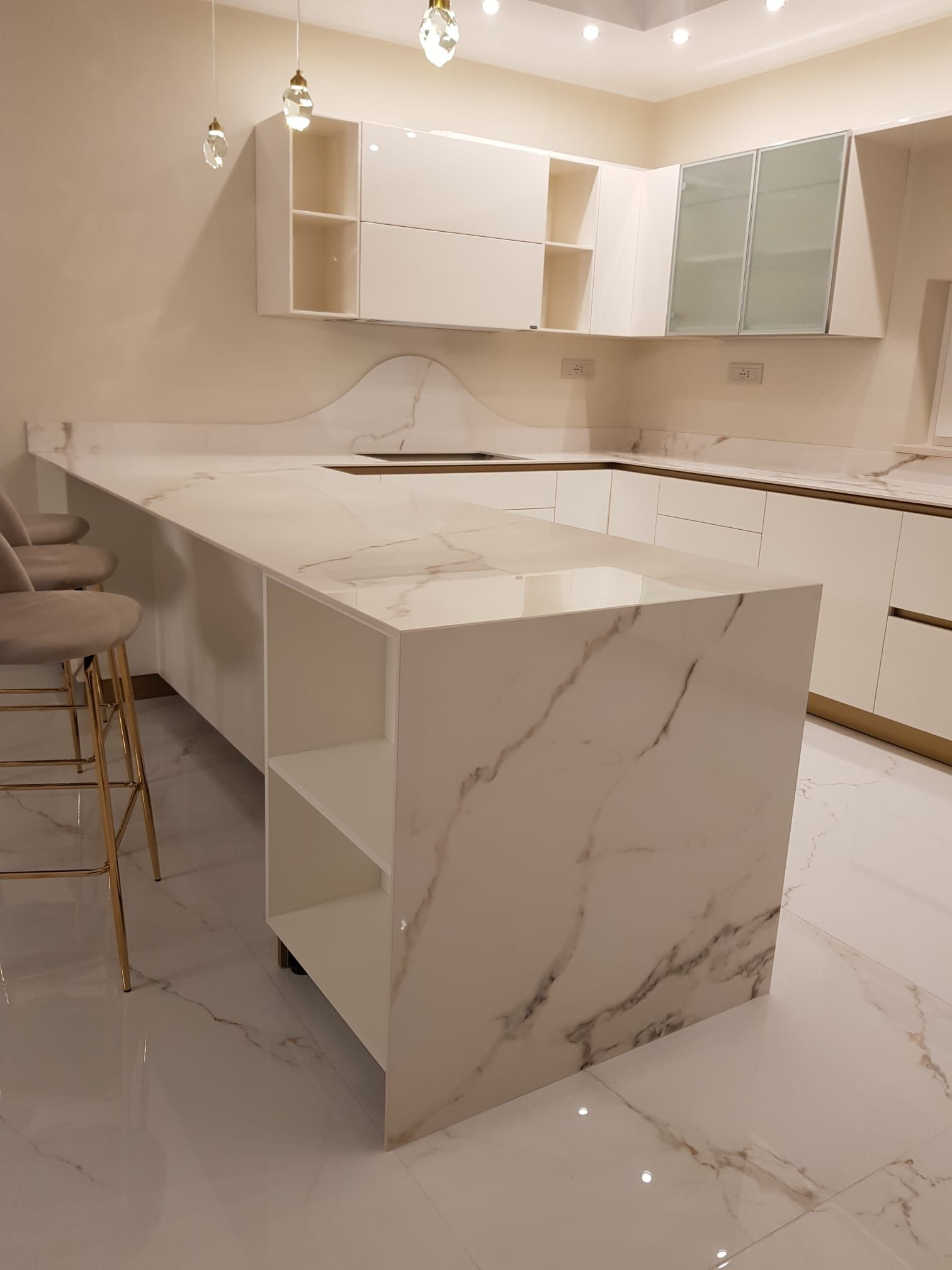 Cucina moderna bianca con isola in marmo, mobili lucidi e pavimento piastrellato.