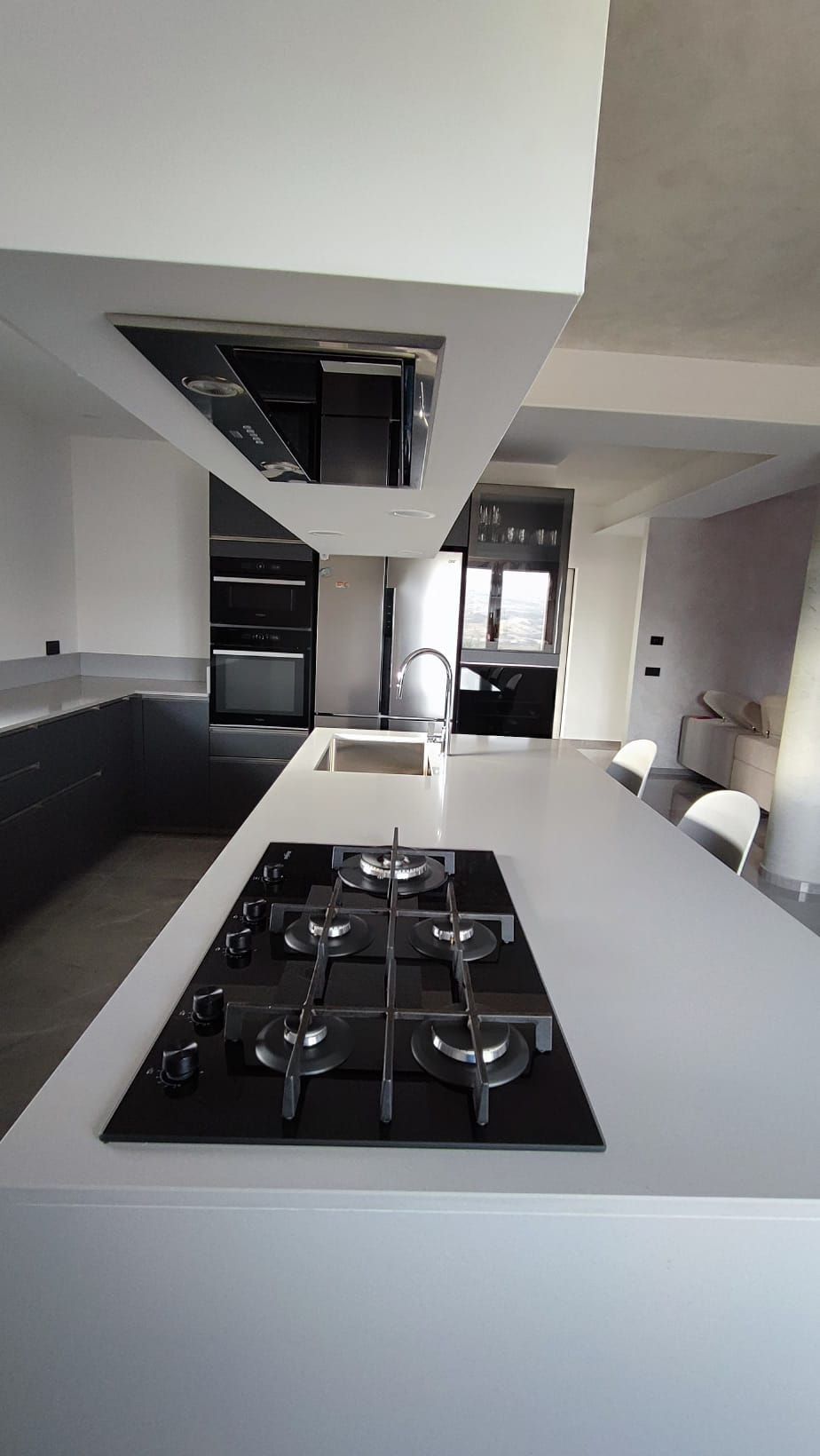 Cucina moderna bianca con isola centrale, piano cottura e mobili neri.