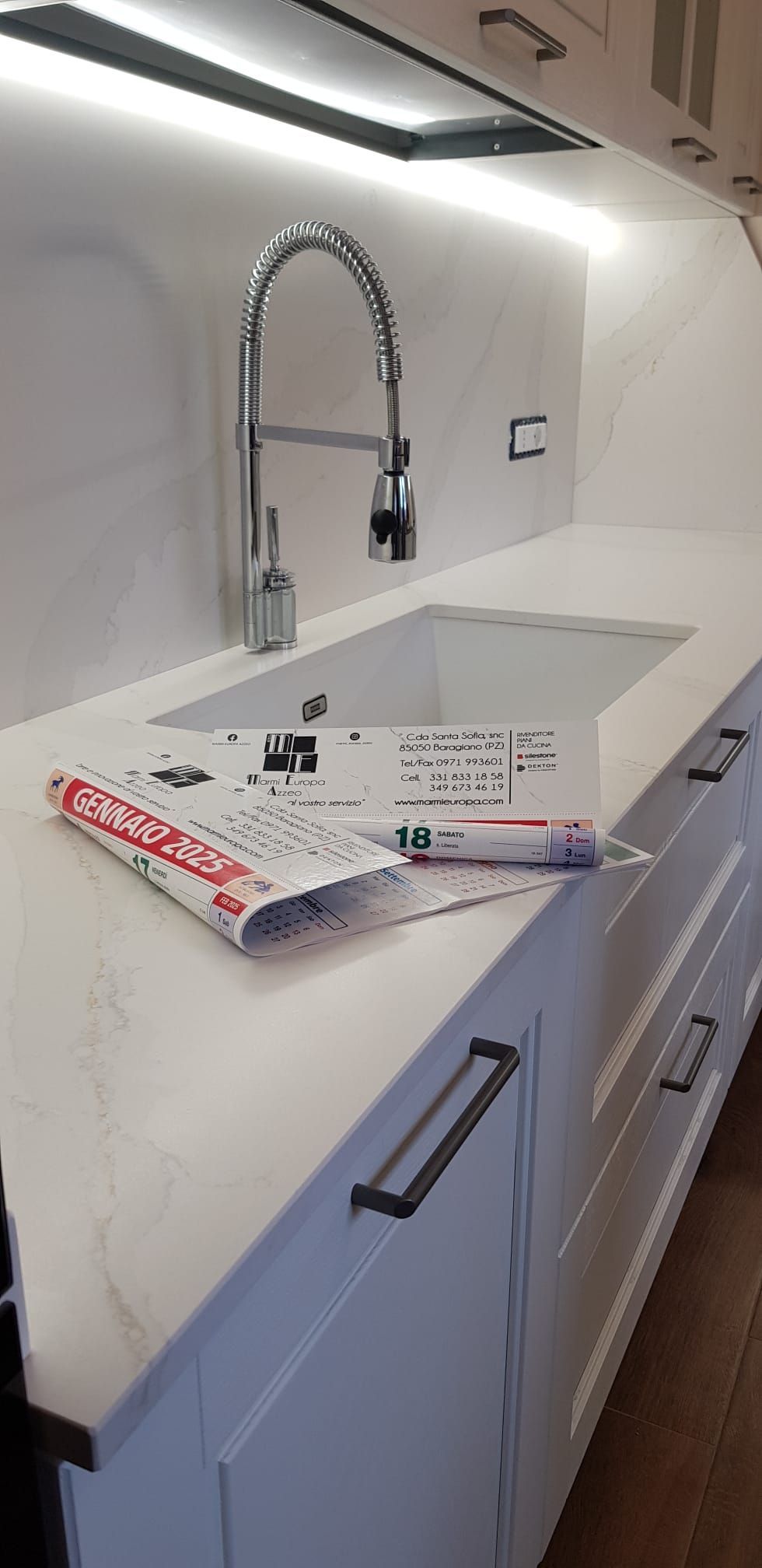 Piano di lavoro da cucina moderno e bianco con lavello, rubinetto e un pacco di carta da regalo sul piano.